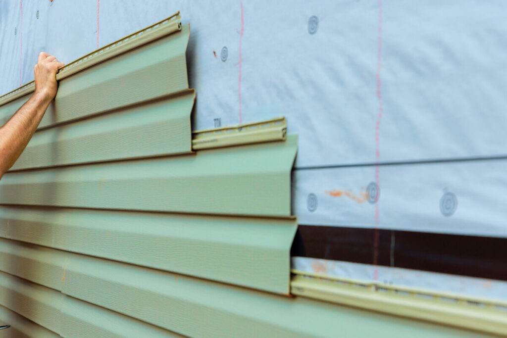 Worker installing green siding on a house exterior during a sunny day