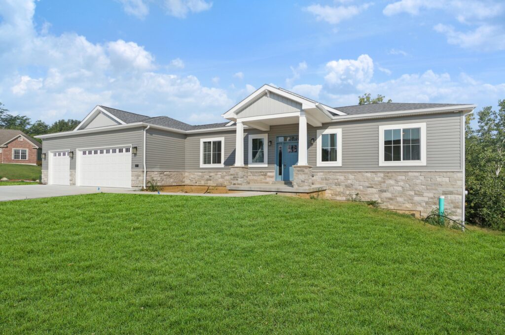 Front view of a gray, single-family home with a stone base, two-car garage, and blue front door on a sunny day.