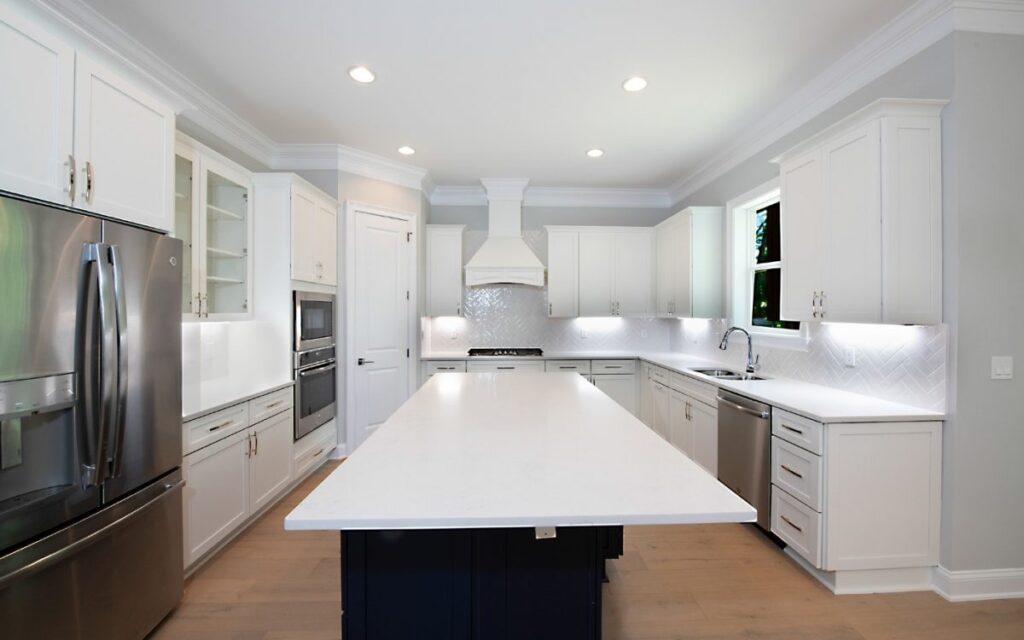 Bright white kitchen with a large central island, stainless steel appliances, and white cabinetry with under-cabinet lighting.